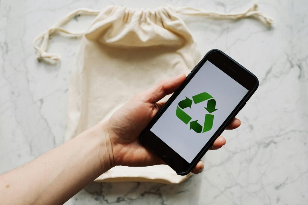 Hand holding smartphone with recycling symbol, promoting eco-friendly lifestyle and reusable bags.